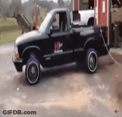 A Black Truck With A White Rim Is Parked In A Parking Lot GIF