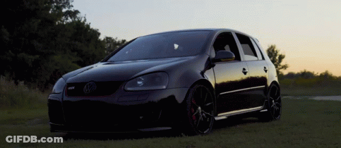 A Black Volkswagen Is Parked In The Grass GIF