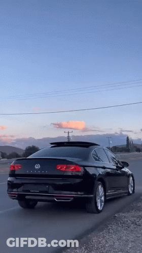 A Black Volkswagen Passat Is Parked On The Side Of A Road . GIF