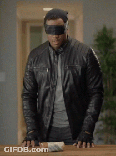 A Blindfolded Man In A Black Leather Jacket Holds A Roll Of Bread GIF
