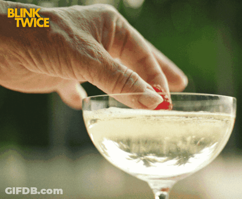 A Blink Twice Ad Shows A Person Putting A Strawberry In A Glass Of Champagne GIF