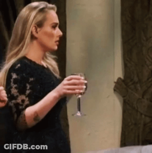 A Blonde Woman In A Black Dress Is Holding A Glass Of Wine . GIF