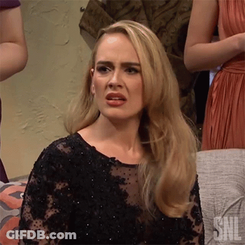 A Blonde Woman In A Black Dress Is Making A Funny Face While Sitting On A Couch . GIF