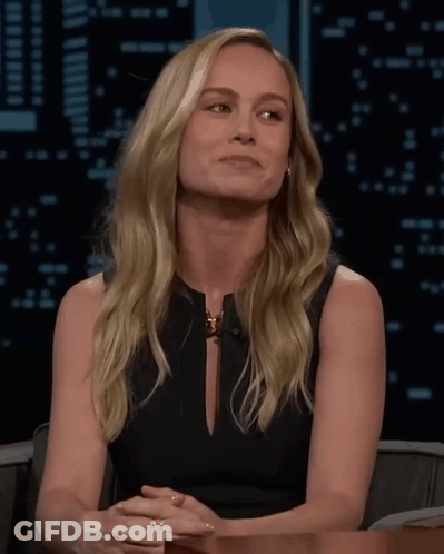 A Blonde Woman In A Black Dress Is Sitting At A Table GIF