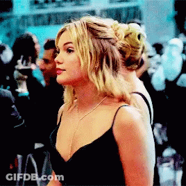 A Blonde Woman In A Black Dress Is Standing In A Crowd GIF