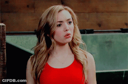 A Blonde Woman In A Red Tank Top Is Standing In Front Of A Wooden Fence GIF