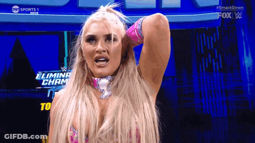 A Blonde Woman Is Standing In Front Of A Sign That Says Eliminate Champ GIF