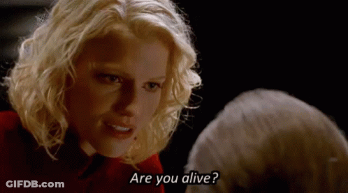 A Blonde Woman Is Talking To A Man In A Dark Room And Asking If He Is Alive . GIF