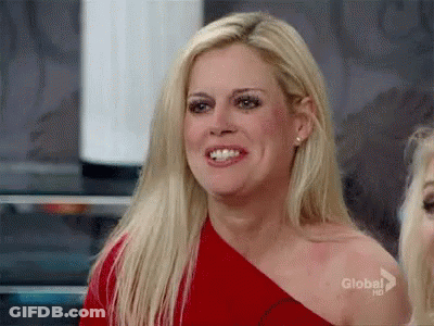 A Blonde Woman Is Wearing A Red One Shoulder Top And Smiling . GIF
