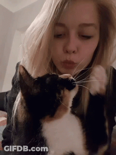 A Blonde Woman Kisses A Black And White Cat On The Nose GIF