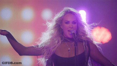 A Blonde Woman Singing Into A Microphone With Her Tongue Out GIF