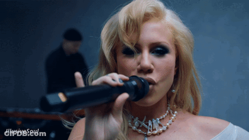 A Blonde Woman Singing Into A Microphone With The Words Illusive Soul Behind Her GIF