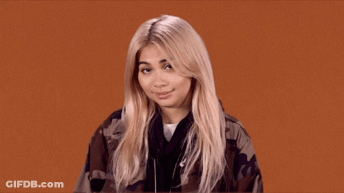 A Blonde Woman Wearing A Camouflage Jacket Looks At The Camera GIF