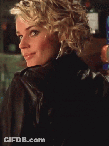 A Blonde Woman Wearing A Leather Jacket And A Blue Top Smiles GIF