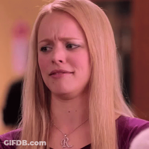 A Blonde Woman Wearing A Necklace With The Letter R On It Is Making A Funny Face . GIF