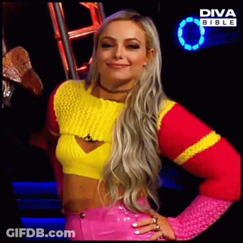 A Blonde Woman Wearing A Yellow And Pink Sweater And Pink Pants Is Standing In Front Of A Diva Bible Sign GIF
