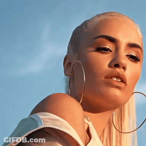 A Blonde Woman Wearing Hoop Earrings Looks At The Camera GIF