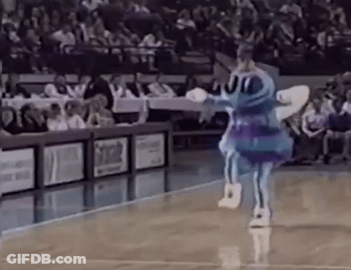 A Blue And Purple Mascot Is Dancing On A Basketball Court In Front Of A Crowd . GIF