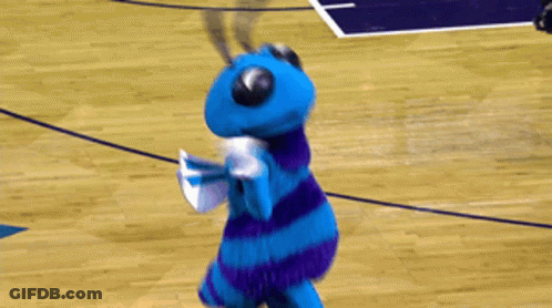 A Blue And Purple Mascot Stands On A Basketball Court GIF