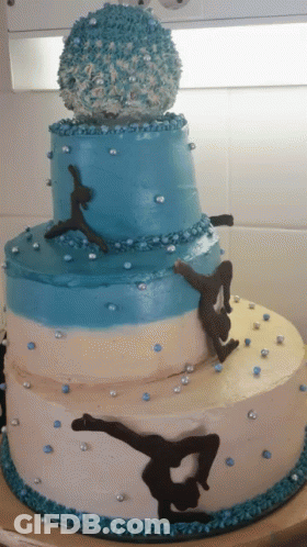 A Blue And White Cake With A Gymnast On Top GIF