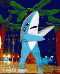 A Blue And White Shark Costume Is Standing On A Stage GIF