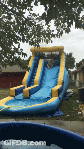 A Blue And Yellow Inflatable Water Slide Is Sitting In A Backyard GIF