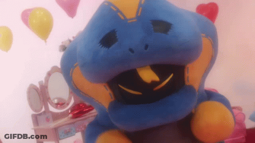 A Blue And Yellow Stuffed Animal Is Sitting In Front Of A Vanity With Balloons In The Background GIF