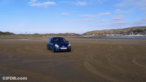 A Blue Car Driving On A Sandy Beach With A License Plate That Says Ykp Xkf GIF
