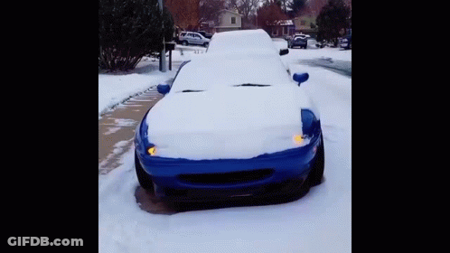 A Blue Car Is Covered In Snow On A Snowy Street GIF