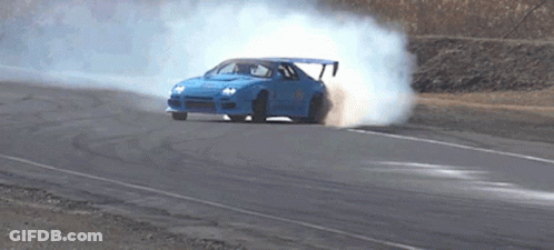 A Blue Car Is Drifting On A Road And Smoke Is Coming Out Of The Tires GIF