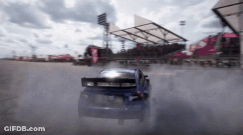 A Blue Car Is Drifting On A Track With Smoke Coming Out Of The Tires GIF