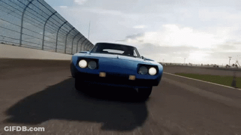 A Blue Car Is Driving Down A Race Track With A Fence In The Background GIF
