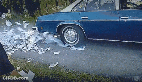 A Blue Car Is Driving Down A Road With A Flat Tire And Smoke Coming Out Of It . GIF