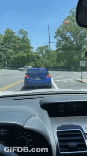 A Blue Car Is Driving Down A Street With A Sign That Says Y On It GIF