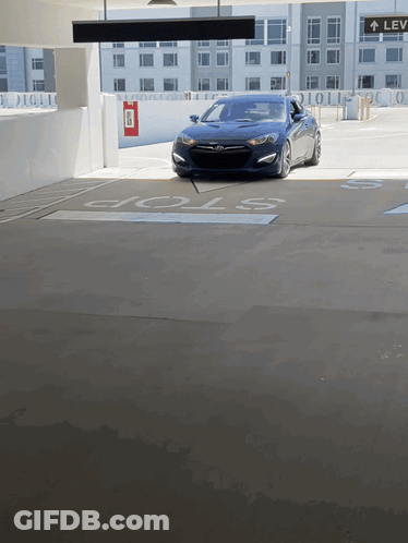 A Blue Car Is Parked In A Parking Garage With A Stop Sign GIF