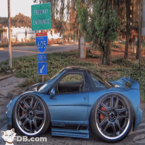 A Blue Car Is Parked In Front Of A Green Freeway Entrance Sign GIF