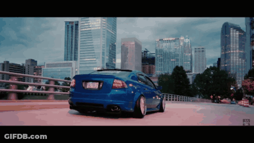 A Blue Car Is Parked On A Bridge In Front Of A Skyline GIF