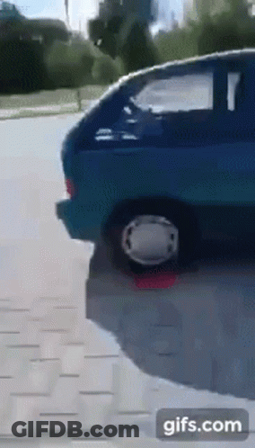 A Blue Car Is Parked On The Side Of The Road With A White Wheel GIF