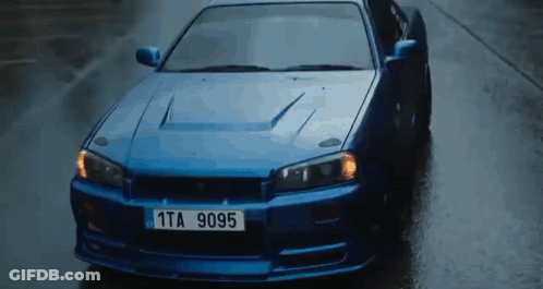 A Blue Car With A License Plate That Says 1Ta 9095 Is Driving Down A Wet Street . GIF