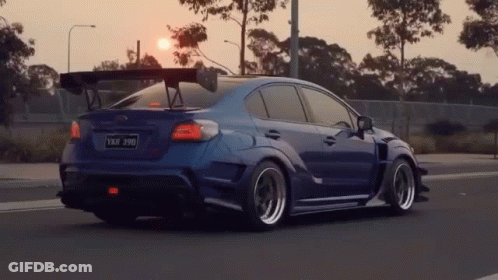 A Blue Car With A Spoiler On The Roof Is Driving Down A Road . GIF