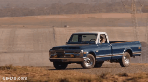A Blue Chevrolet Truck Is Driving Down A Dirt Road In The Desert GIF