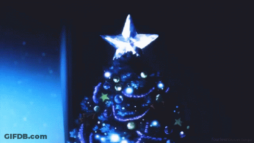 A Blue Christmas Tree With A Star On Top Is Displayed In A Dark Room GIF