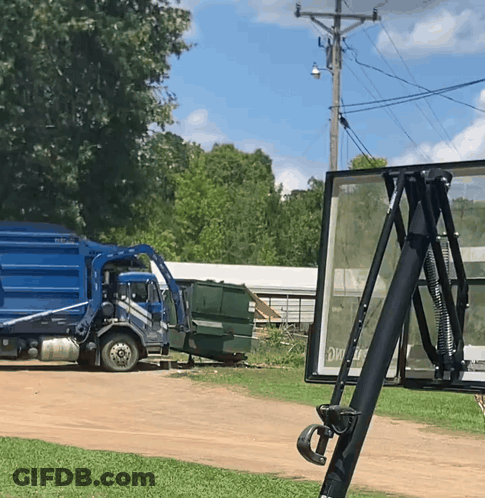 A Blue Garbage Truck Is Parked On A Dirt Road Next To A Sign That Says Exit GIF