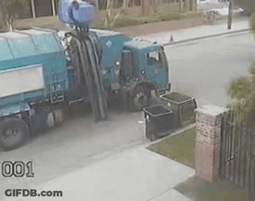 A Blue Garbage Truck Is Parked On The Side Of The Road Next To A Black Trash Can . GIF