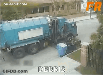 A Blue Garbage Truck Is Parked On The Side Of The Road Next To A Building . GIF