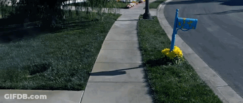 A Blue Mailbox On The Side Of A Sidewalk With A Yellow Flower GIF