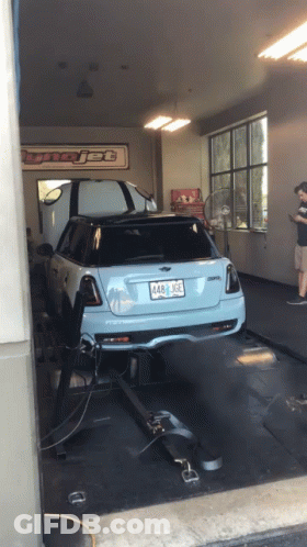 A Blue Mini Cooper Is Being Tested In A Garage With A Sign That Says Tunejet GIF