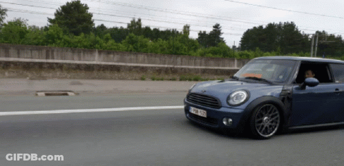A Blue Mini Cooper Is Driving Down A Road With A License Plate That Says ' Nzl 929 ' On It GIF