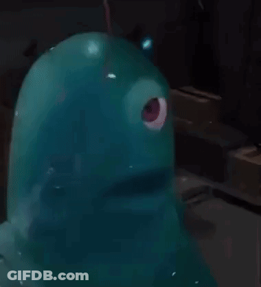 A Blue Monster With A Red Eye Is Sitting On A Table In A Dark Room . GIF