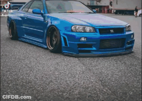 A Blue Nissan Skyline R34 Is Parked On The Side Of The Road . GIF